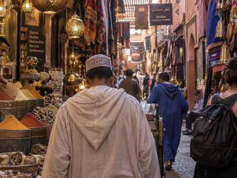 Busy spice market alley with hanging lanterns and open sacks of colorful spices