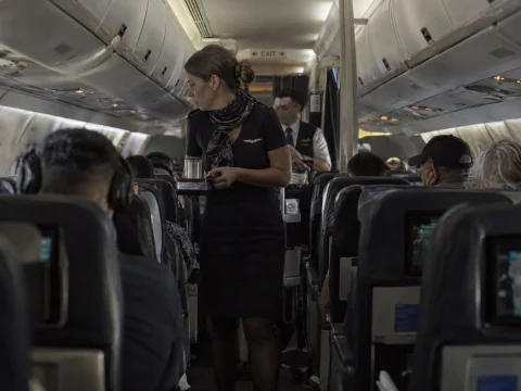 Flight attendant walking down the aisle of a full airplane cabin