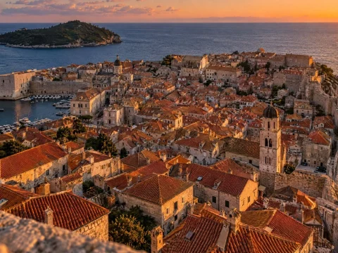 Old walled town with red roofs by the sea at sunset, a small island offshore