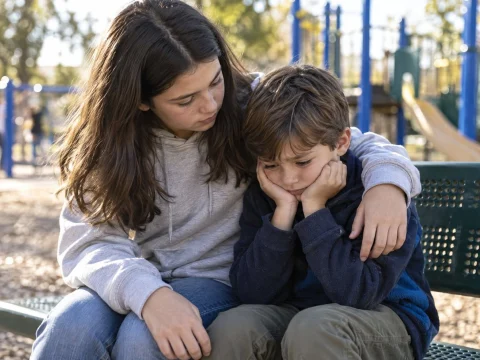 Young child comforting a younger sibling on a playground bench on a sunny afternoon