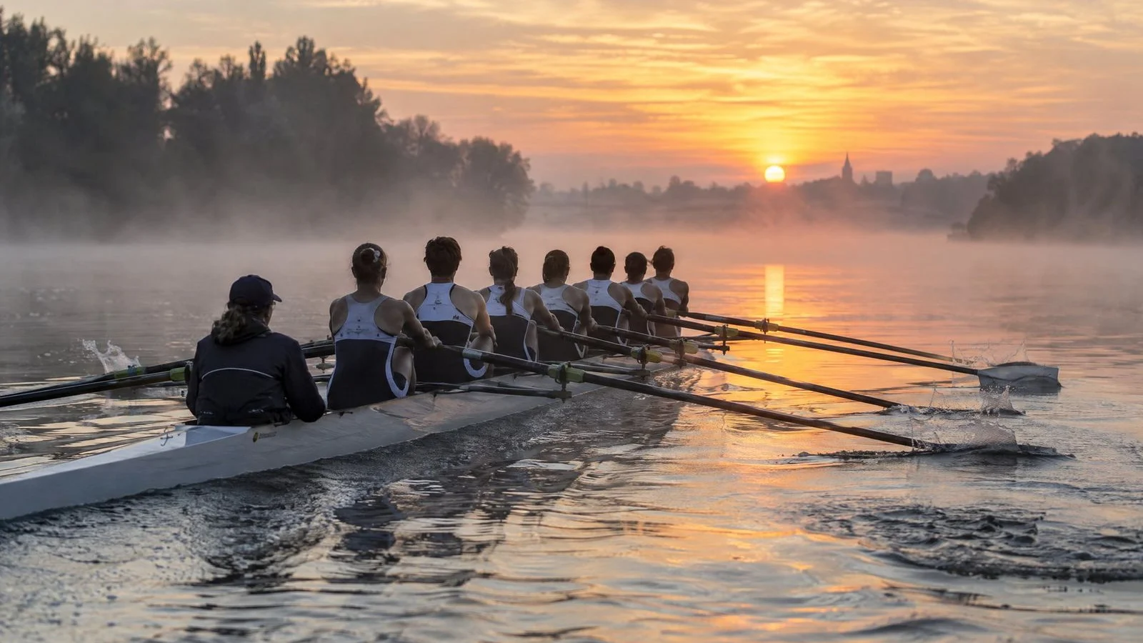 Rowing eight crew gliding on a calm, misty river at sunrise
