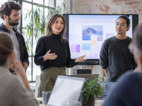 A small startup team presenting to colleagues in a bright loft office in front of a large screen