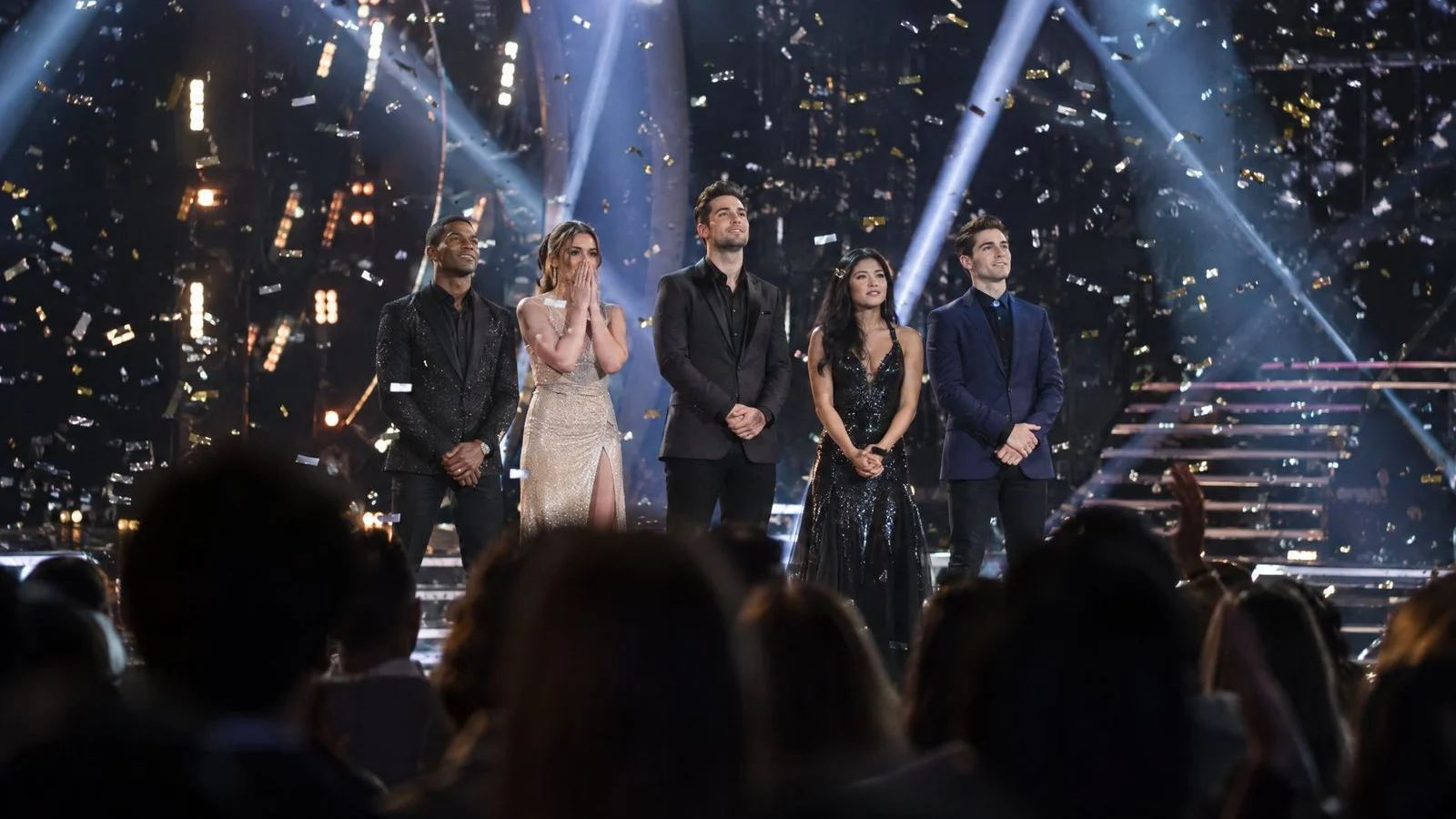 Finalists standing in spotlights on a TV stage as confetti falls over a darkened audience