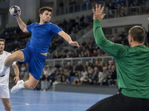 Handball player in a plain jersey jumping to shoot at goal in an indoor arena