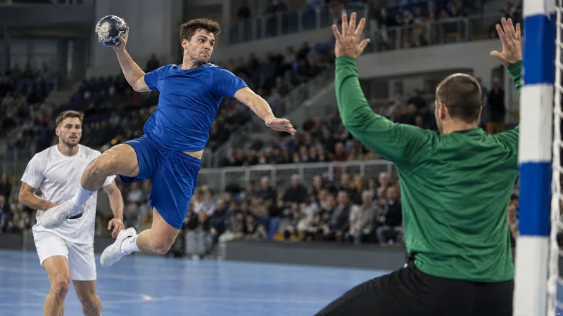 Handball player in a plain jersey jumping to shoot at goal in an indoor arena