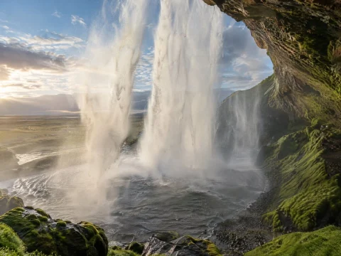 Waterfall seen from behind, framed by the walls of a mossy cave