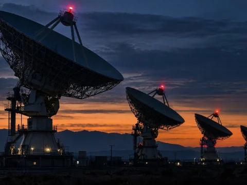 Large radio telescope dishes silhouetted against an orange dusk sky