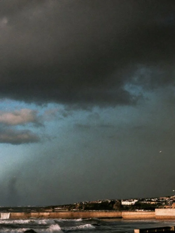 Dark storm clouds over a coastal town as waves crash against a seawall in heavy rain