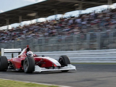 Open-wheel race car speeding past a grandstand on a race track, motion blur