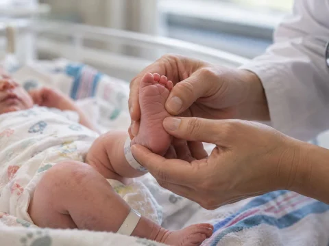 Pediatrician gently examining a newborn baby's foot in a hospital, close-up in soft light