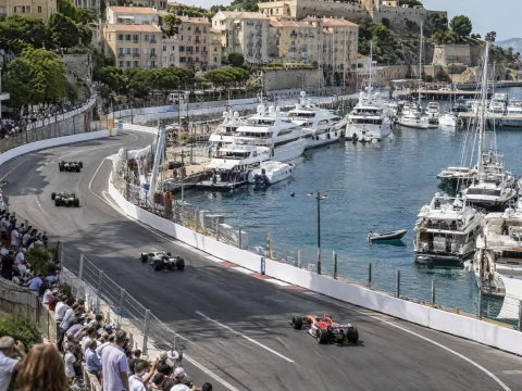 Aerial view of a street circuit with white barriers winding through a seaside harbor town full of yachts