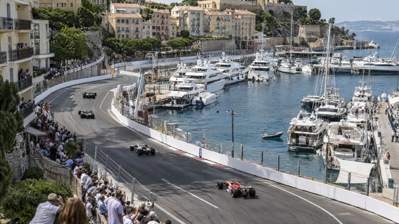 Aerial view of a street circuit with white barriers winding through a seaside harbor town full of yachts