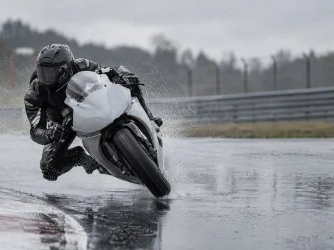Racing motorcycle leaning into a corner on a wet track, throwing up spray under a grey sky