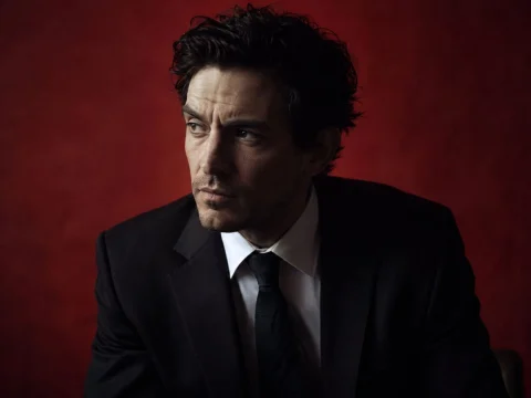 Moody portrait of an actor in a dark suit against a deep red background in cinematic light