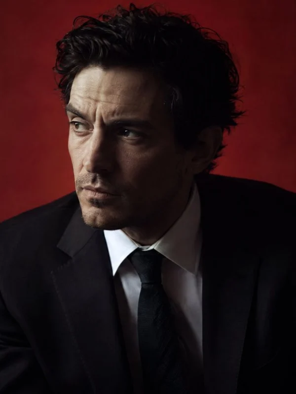 Moody portrait of an actor in a dark suit against a deep red background in cinematic light