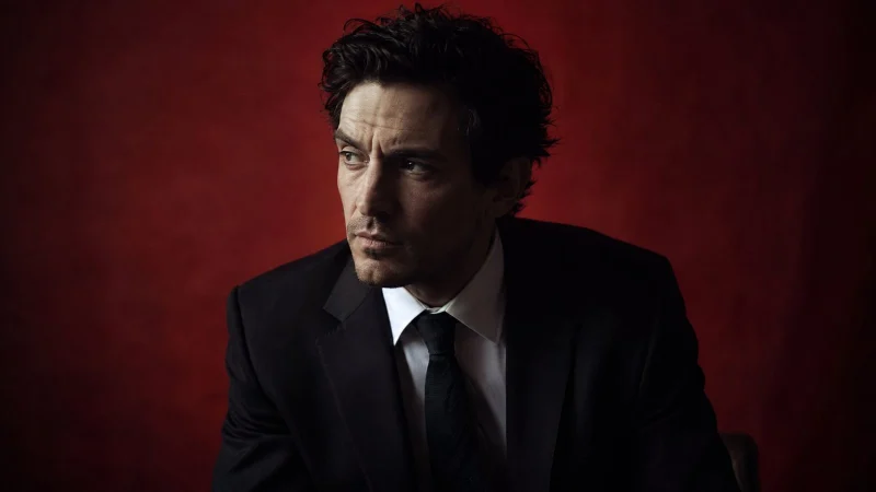 Moody portrait of an actor in a dark suit against a deep red background in cinematic light