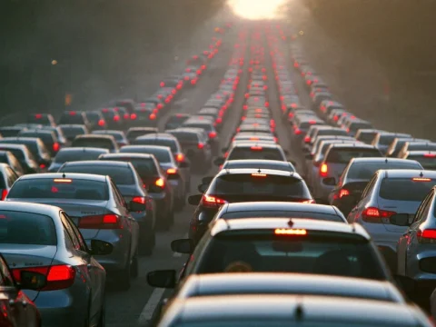 Long line of cars with red brake lights on a multi-lane city avenue in low morning sun