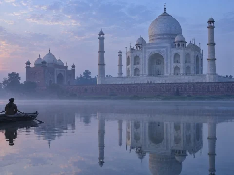 White marble mausoleum reflected in a calm river at dawn, with a small rowing boat