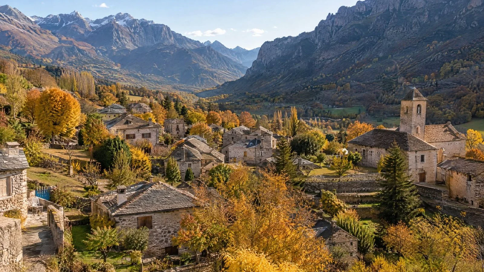 Aerial view of a valley village with stone houses among autumn trees beneath mountains on a sunny day