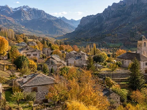 Aerial view of a valley village with stone houses among autumn trees beneath mountains on a sunny day