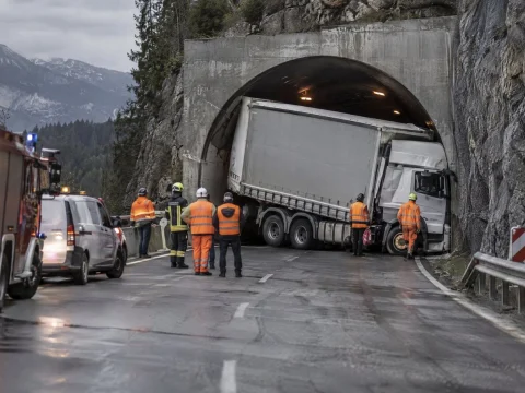 Large truck stuck at a mountain tunnel entrance with emergency vehicles and workers in orange vests
