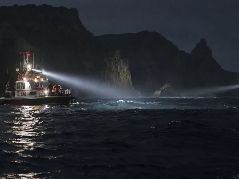 Rescue boat sweeping searchlights over a dark sea near steep cliffs at night