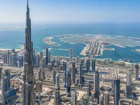 Aerial view of a coastal city with a very tall tower and a palm-shaped island in the sea