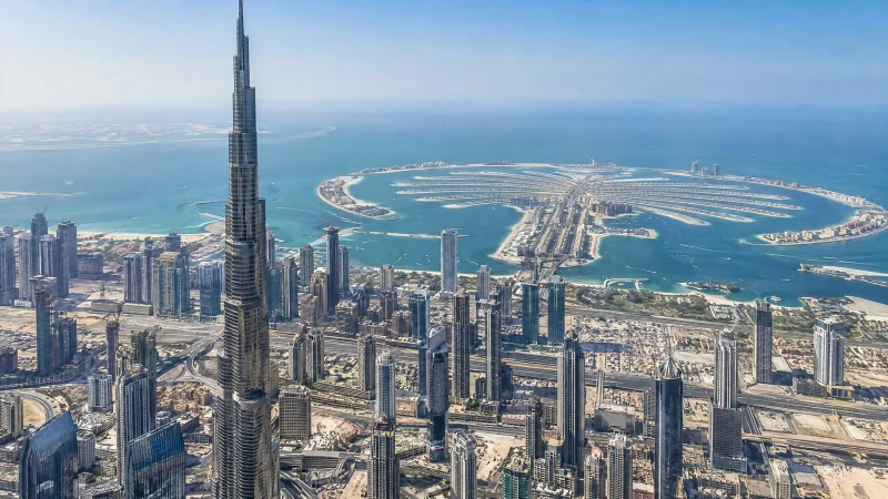 Aerial view of a coastal city with a very tall tower and a palm-shaped island in the sea